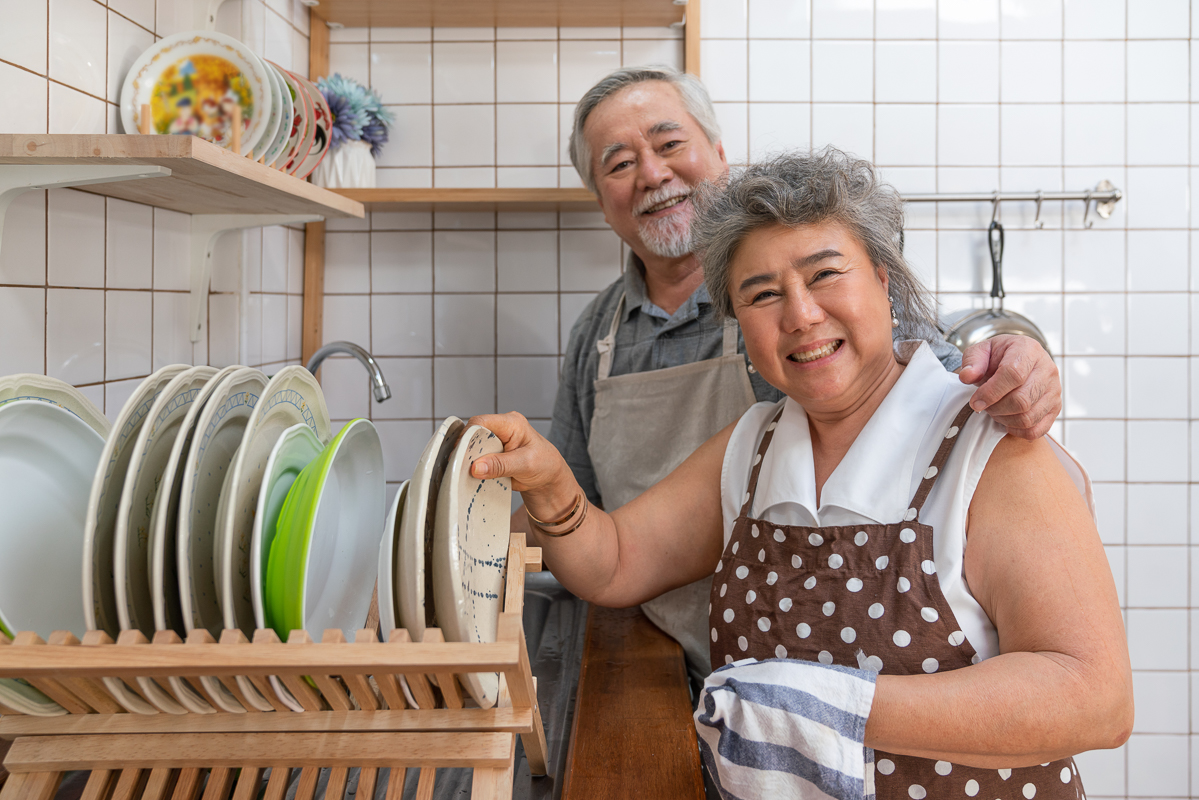 Happy couple Asian elder smiling and washing dishes in the sink together in the kitchen at home