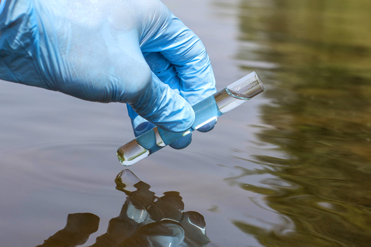 Sample water from the river for analysis. Hand in glove holding a test tube