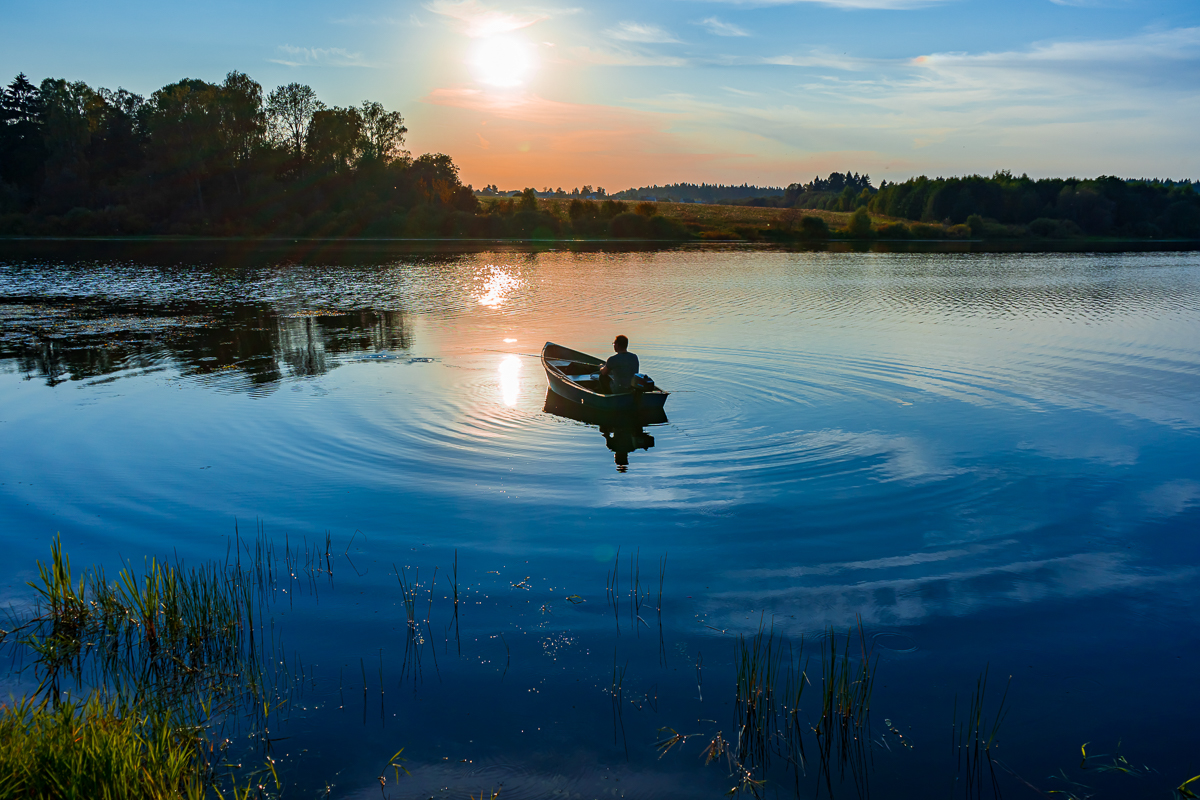 Mature caucasian man fishing in a small boat with a motor at sunset on the lake